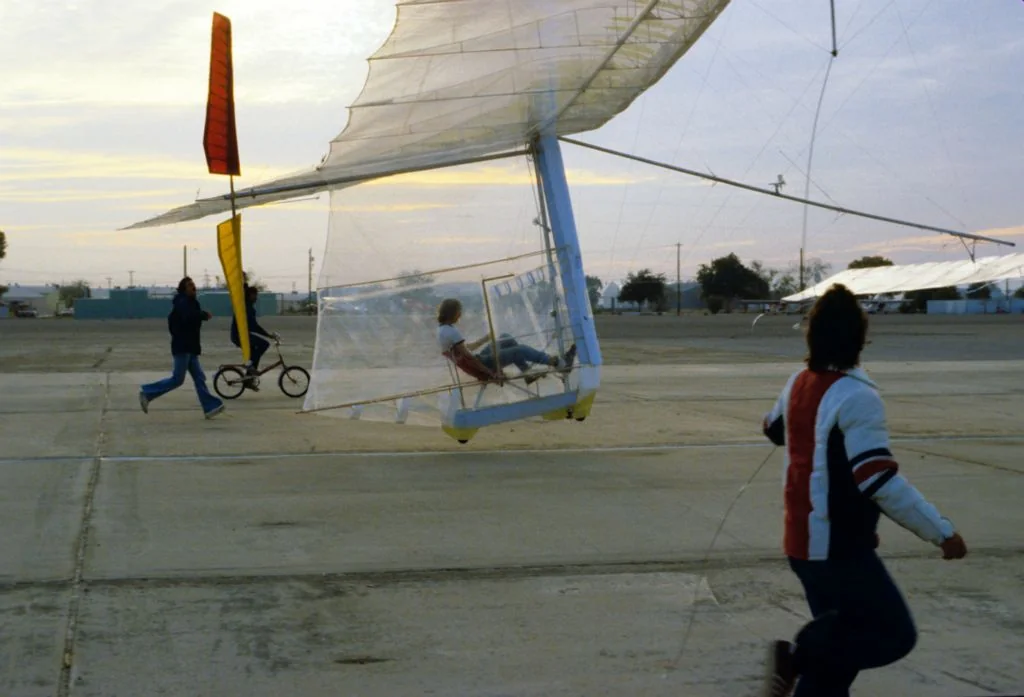 Bryan Allen pedals the Gossamer Condor above the runway while members of the team run and cycle alongside, September 24, 1977.