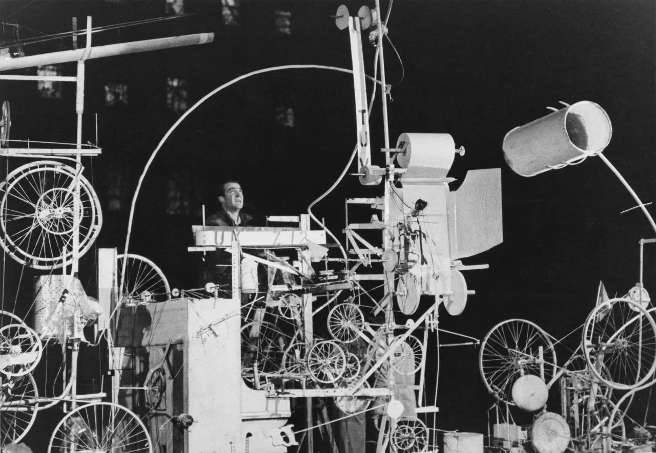 Jean Tinguely stands amid the white-painted wheels, drums and machinery of Homage to New York during its 1960 performance.