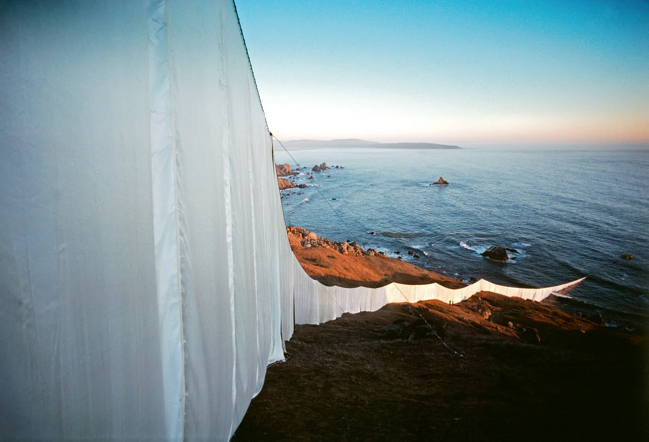 The white fabric of Running Fence descends a sunlit California hillside toward the Pacific Ocean.